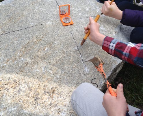 elementary students carving compass rose on granite boulder with hammer and chisel during Drystone Joe artist residency